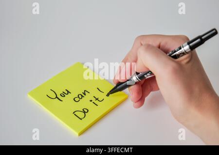A hand holding a black marker finishes writing You can do it on a yellow sticky note. The image represents handwritten motivation, personal encouragem Stock Photo
