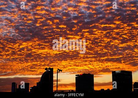 Shanghai city skyline silhouettes beneath a dramatic fiery orange sunset sky filled with dense altocumulus clouds. Stock Photo