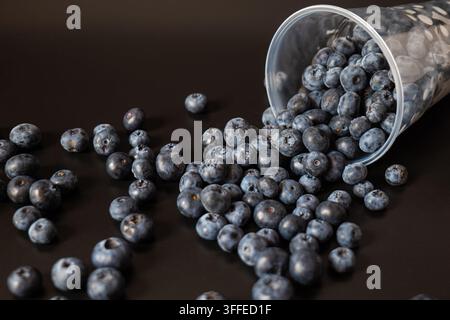 A transparent cup rests on its side with focus on its opening and nearby berries. The angled perspective highlights depth, texture, and abundance. Stock Photo