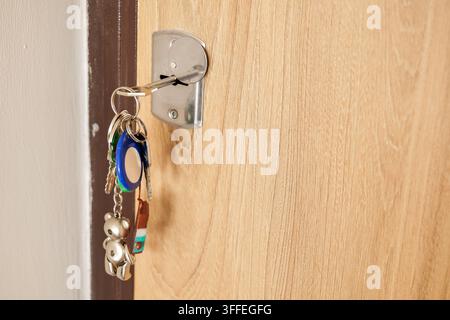 A set of metal keys hangs from a keyring inserted into a lock on a light wood interior door. Home access and door security concept Stock Photo