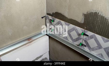 Close up of tiling work in progress. DIY home improvement or professional construction concept. Grey and white geometric pattern on wall. Interior fin Stock Photo