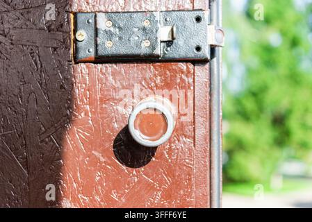 A close-up view of an outdoor brown OSB wooden utility shed door featuring a heavy-duty metal slide latch and a round handle against a blurred green b Stock Photo