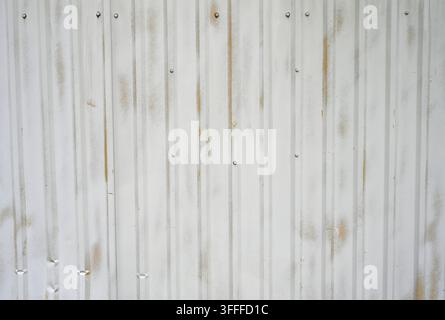 White painted textured corrugated tin metal with stippling texture and worn areas revealing yellow paint Stock Photo