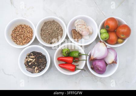 Assorted whole spices and dried herbs arranged in small bowls on a clean white marble surface Stock Photo