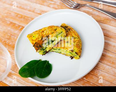 Few small pieces of fluffy egg and spinach omelet are on plate. Dish is decorated with two young and delicate spinach leaves Stock Photo
