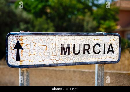 A rustic wooden framed chalkboard propped against a black wrought iron fence with dense green foliage behind it. White chalk handwriting fills the boa Stock Photo