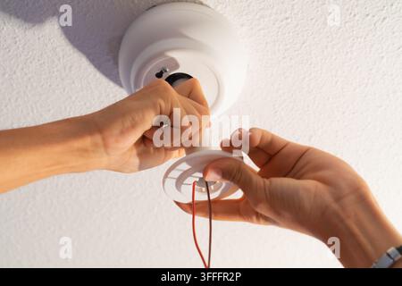 Close-up of a technician's hands installing the support of a ceiling lamp with exposed electric wires during a renovation. Stock Photo