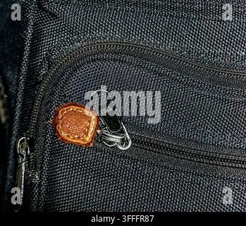 Macro close-up of a black fabric bag featuring a metal zipper, clasp, and distinctive brown leather zipper pull Stock Photo