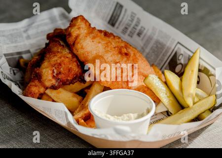 Plate of fish and chips, the famous British classic consisting of fish fillets in golden batter and french fries, served with a small bowl of sauce Stock Photo