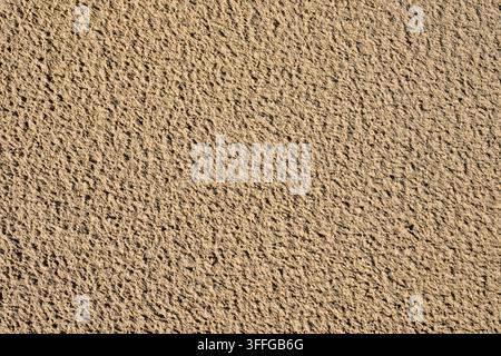 Close-up of wet beach sand after rain, showing natural textured patterns, fine grains and irregular surface details shaped by water and weather Stock Photo
