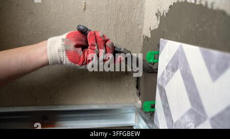 Home improvement or construction site scene. Handyman lays decorative tile using mortar and green plastic spacers for alignment. Professional tiling a Stock Photo