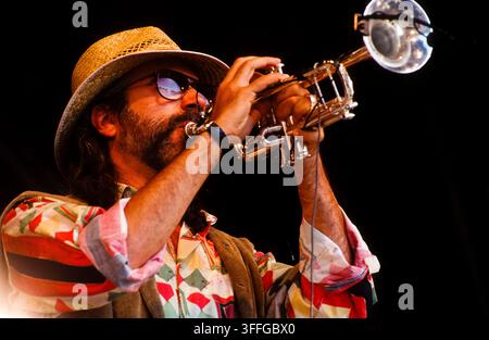 LONDON, UK - JUNE 27, 1993: American jazz fusion trumpeter and composer Randy Brecker performs live onstage with the Brecker Brothers band during the Jazz on a Summer's Day festival held at Alexandra Palace in London, United Kingdom on June 27, 1993. Brecker is captured in a close up profile shot blowing his trumpet into a clip on stage microphone while wearing a straw fedora hat, dark sunglasses, and a vibrant, geometric-patterned shirt under a brown vest. This archival colour music photograph preserves a striking moment from the legendary duo's nineties reunion tour. Stock Photo