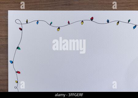 Hand drawn string of small colored holiday light bulbs on textured white paper placed over wooden table background with top Stock Photo