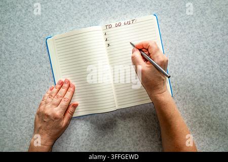 Person writing a to do list in a lined notebook with pen and hands on a table Stock Photo