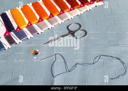 Close-up of embroidery threads, needle and scissors on aida cross stitch fabric with stitching Stock Photo