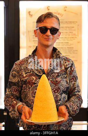 A happy tourist holds a unique, giant, cone-shaped arancino. Famulari Bakery in Messina ,Sicily, September 11, 2026. Stock Photo