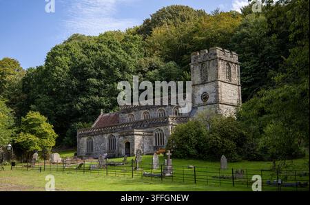 Stone Parish Church with tower and surrounding graveyard nestled against wooded hillside St Peters Church Stourhead Stock Photo
