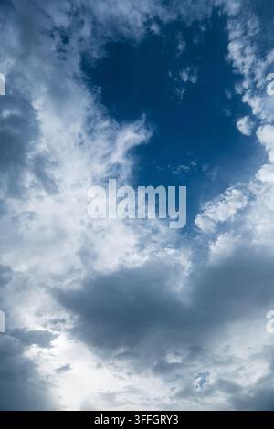 Dramatic overcast weather pattern featuring textured white cumulus clouds transitioning into dark gray rain storm layers against a vibrant blue atmosp Stock Photo