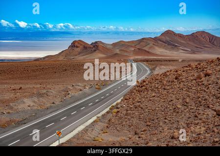 A long remote road traversing the arid landscape of the Atacama Desert in northern Chile, with the vast Salar de Atacama salt flat. Stock Photo