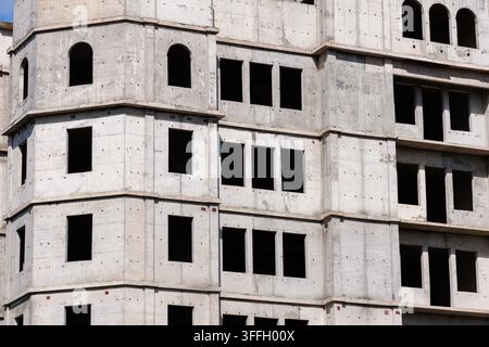 A detailed exterior view of an unfinished multi-story concrete residential building, featuring empty rectangular and arched window openings under brig Stock Photo