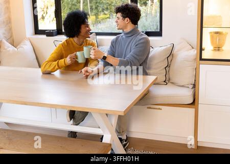 African American couple sitting at home touching hands, wearing sweaters and holding green mugs Stock Photo