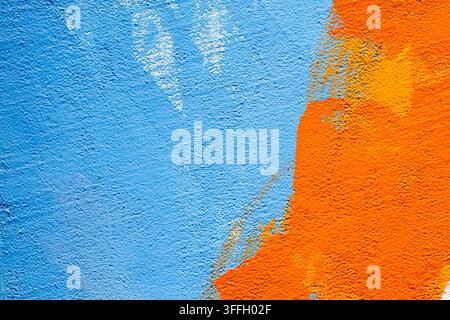 A close-up view of a rough concrete wall surface painted with vibrant blue and bright orange colors, creating an abstract textured background with vis Stock Photo