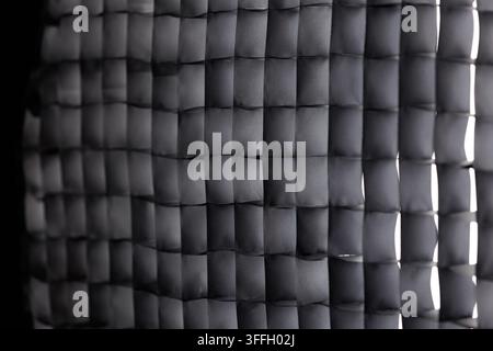 A close-up macro shot of a black fabric honeycomb grid for a studio photography softbox, featuring selective focus and a gradient of light from the ri Stock Photo