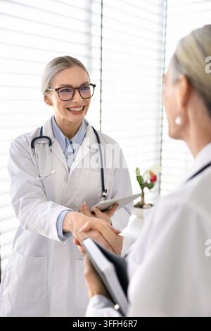 Smiling female doctor handshake with colleague during meeting in clinic Stock Photo