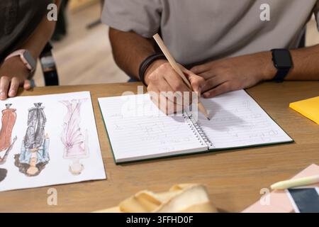 African American designers sketching on spiral notebook with pencil and swatches at wooden table Stock Photo