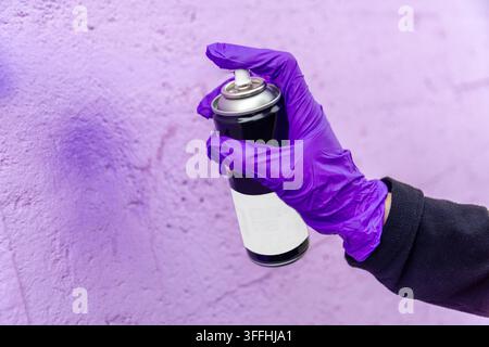Hand in purple glove spraying paint on wall Stock Photo