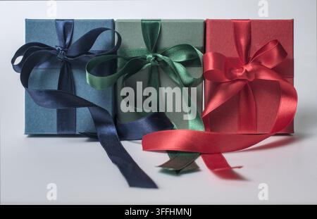 Three colored gift boxes with ribbons on white table. Stock Photo