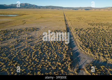 A straight and unpaved road goes in a straight line across desert landscape in the Great Basin desert in California, USA. Stock Photo
