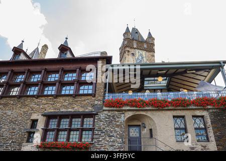Medieval castle architecture with stone walls, wooden timber-framed windows, and a scenic terrace decorated with blooming red geranium flowers under a Stock Photo
