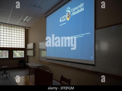 A projector screen displays the University of Manitoba's idle screen, including its crest and wordmark, above a lectern in a lecture theatre inside th Stock Photo