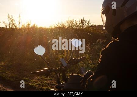 Motorcyclist wearing a protective helmet rides through a swarm of tiny insects on a scenic rural dirt road during a golden hour sunset, ensuring safet Stock Photo