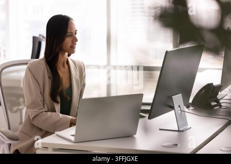 Focused businesswoman analyzing data on laptop in corporate office Stock Photo
