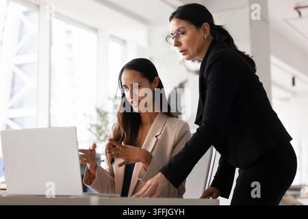 Diverse focused women coworkers reviewing project data on laptop Stock Photo