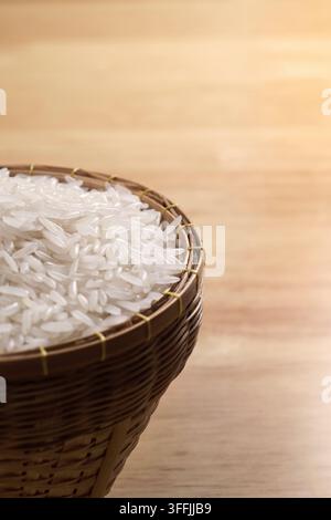 close up shot with empty blurred copy space of raw Thai's jasmine rice in Thai's traditional style bamboo's bowl on wooden dinner table Stock Photo