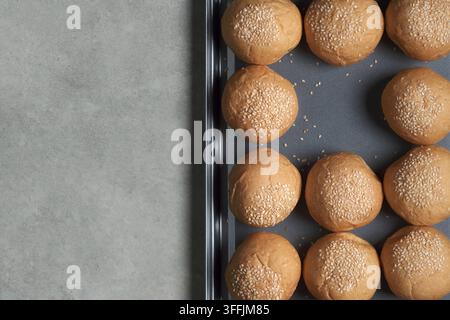 top view shot of many burger breads on the oven tray on rusty kitchen table with empty space of picked up bun for cooking hamburger Stock Photo