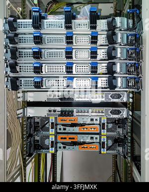 Rear view of servers, switches and storage devices in a rack mounted one above the other. Power and optical cables are visible Stock Photo