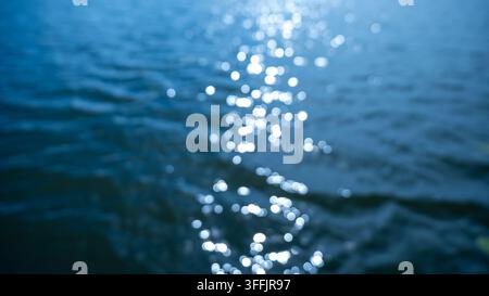 Abstract beautiful bokeh of bright sunlight reflecting on blue water surface. Cinematic blurry sun glares on lake ripples background. High quality pho Stock Photo