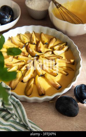 Arranging fresh plum slices on custard batter in a white baking dish Stock Photo