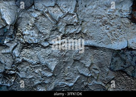 Silver peeling paint is cracking on a textured wall surface. Stock Photo