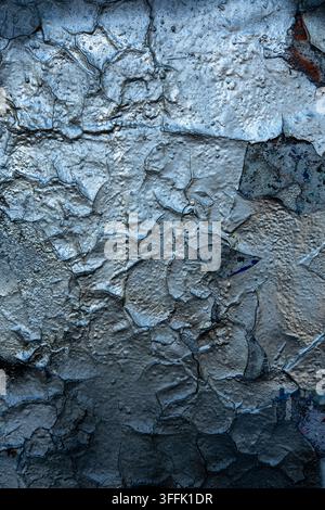 Dark silver peeling paint is cracking heavily on an old weathered wall. Stock Photo
