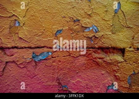 Yellow, orange, and red peeling paint is cracking on a vibrant textured wall. Stock Photo