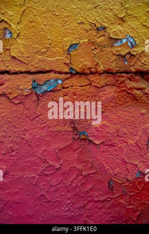 Vibrant gradient of yellow, orange, and red peeling paint is cracking on a textured wall. Stock Photo