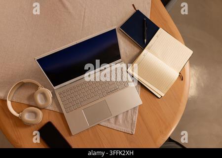 Open silver laptop with dark screen is sitting diagonally on round wooden table with notebooks Stock Photo