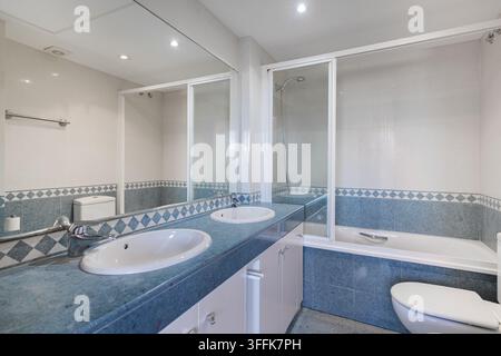 Modern bathroom with blue mosaic tiles double sinks bathtub and large mirrors creating bright spacious interior Stock Photo