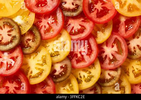 Fresh tomatoes in different colors sliced into juicy pieces, photographed from above in a full frame macro view. Vibrant red, yellow, green and brown Stock Photo