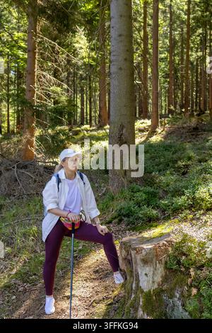 Woman rests during hiking break with trekking poles in pine forest of Karkonosze National Park. Concept of solo female hiking adventure and outdoor re Stock Photo
